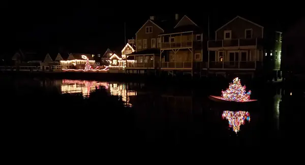 A lit Christmas tree in a dory reflected in the harbor at night